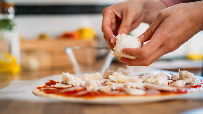 hands adding mozzarella to uncooked pizza