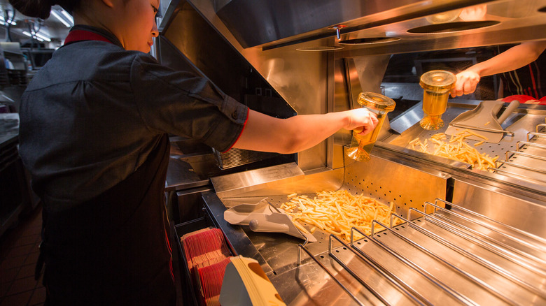 Worker adding salt to french fries