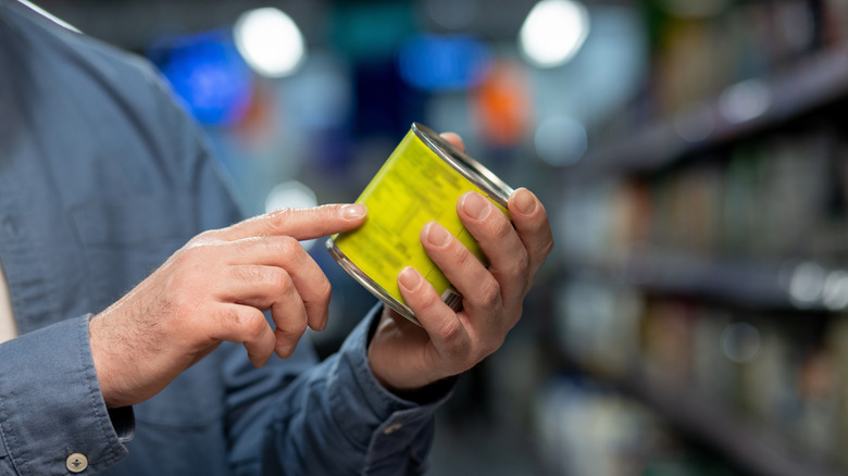 Person reading ingredient label on can in grocery store