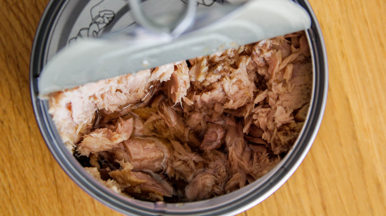 Half-open can of chicken on wooden surface