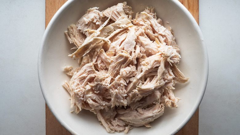 Shredded chicken in white bowl on cutting board