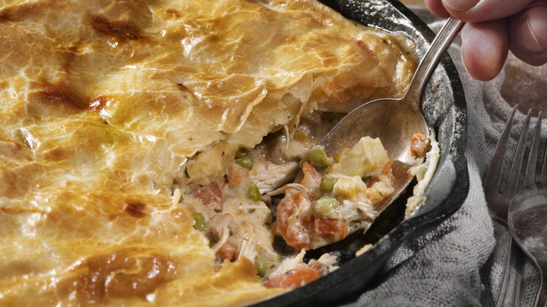 Spoon scooping out filling of chicken pot pie in cast iron skillet