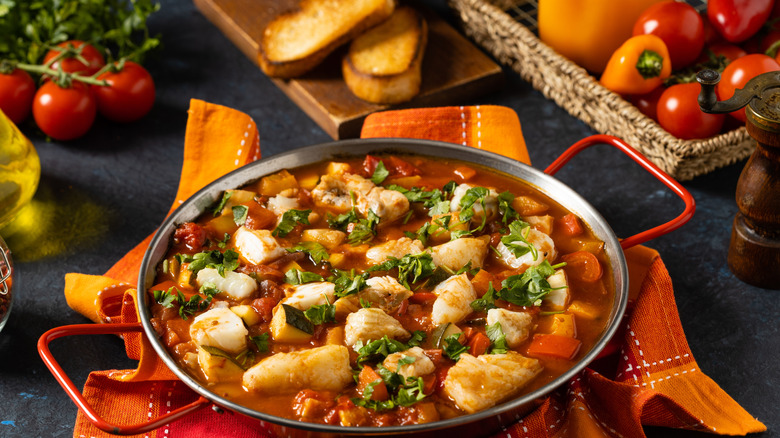 fish stew in pan surrounded by fresh produce and bread