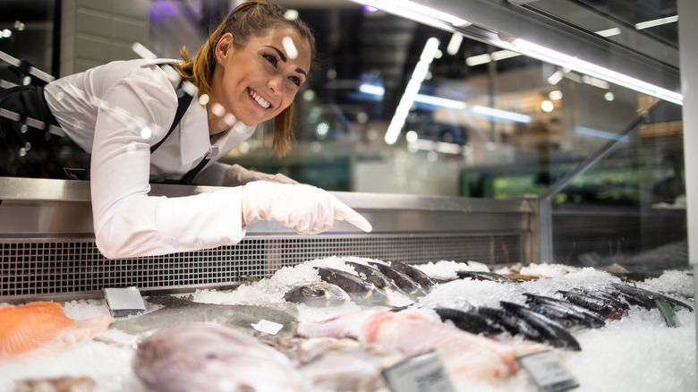 woman pointing at frozen fish in counter