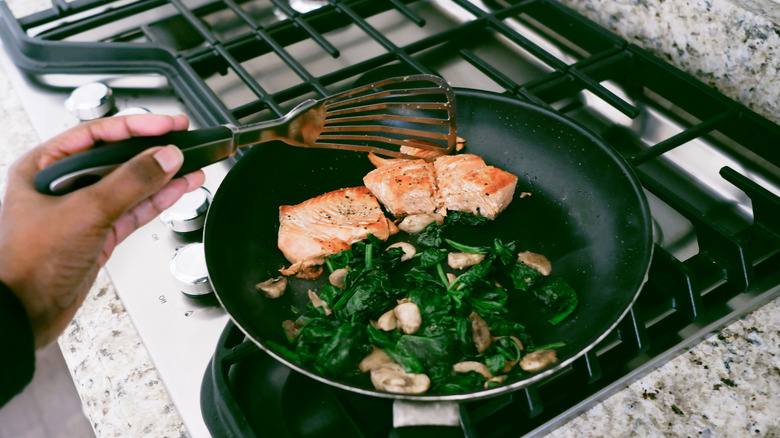 cooking salmon in pan with spinach and mushrooms