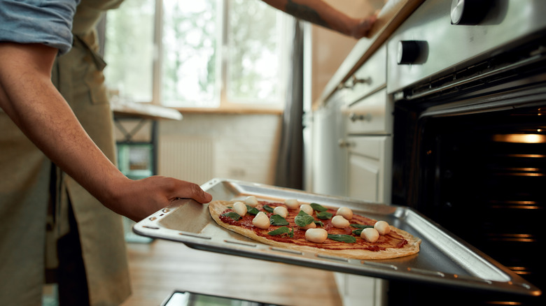 man putting pizza in oven