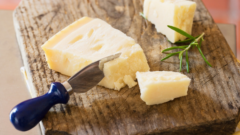 Parmesan on cutting board with knife and rosemary