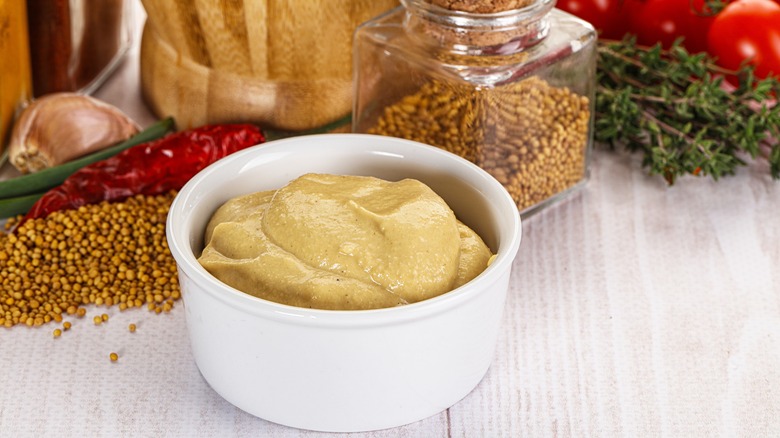 Bowl of Dijon mustard with mustard seeds and peppers in background