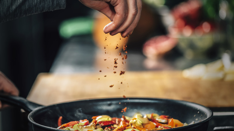 sprinkling spices over vegetables in pan