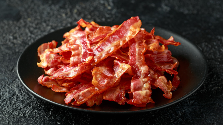 a black plate piled high with strips of crisp bacon on a black backgound