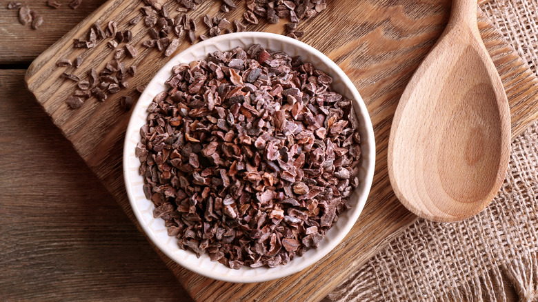 a white bowl full of cocoa nibs on a wood surface