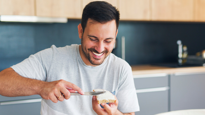 man spreading cheese on bread inside kitchen