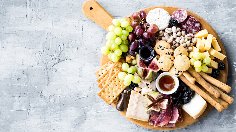 cheese board with salami, crackers, round cheese, nuts and cookies