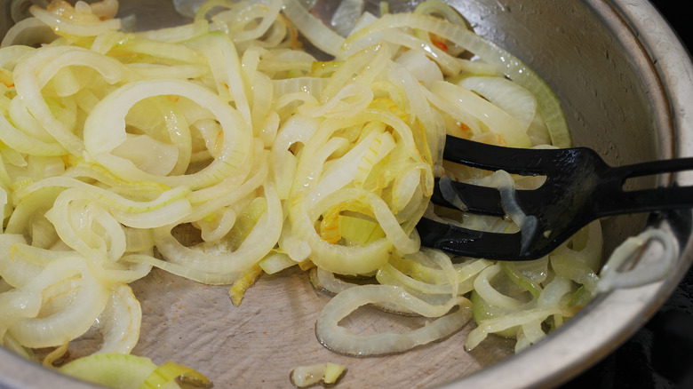 stirring sliced onions in pan