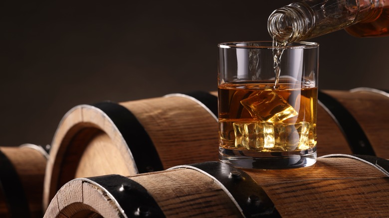 Whiskey being poured into glass atop barrel