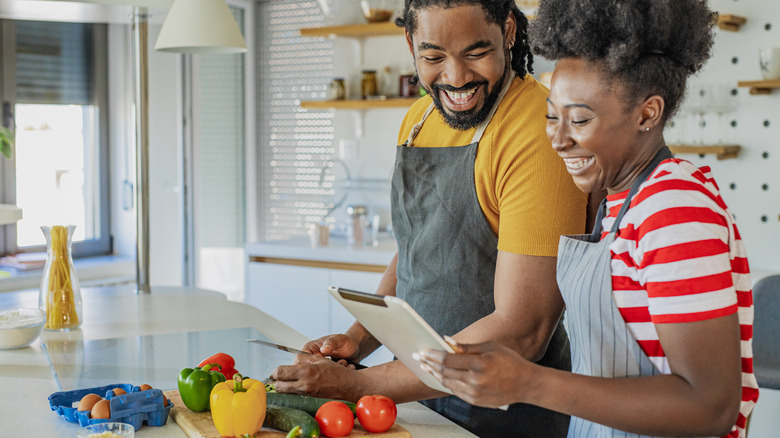 couple checking tablet and cutting vegetables