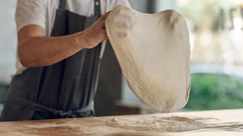 person stretching pizza dough