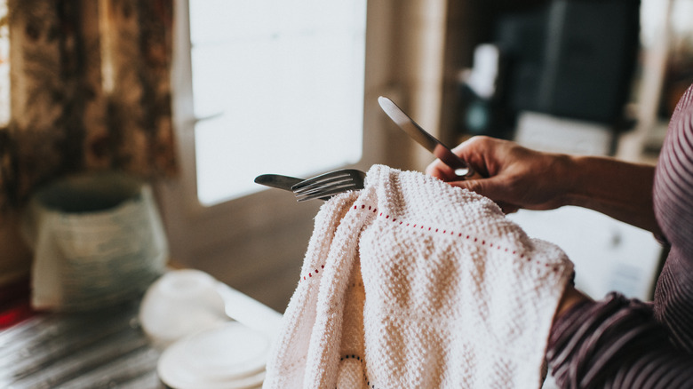 woman washing silverware with cloth