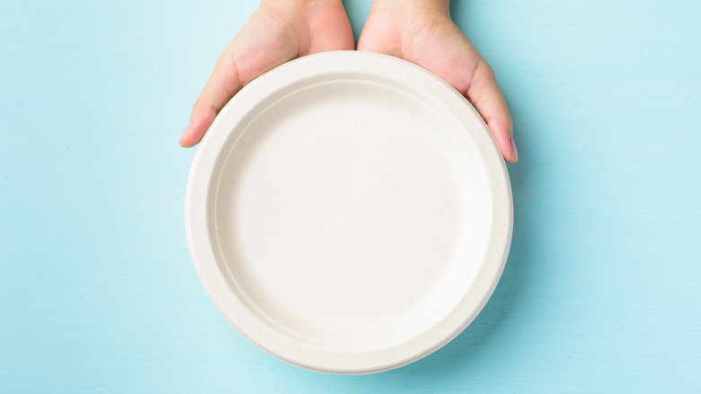 hands holding white disposable plate blue background