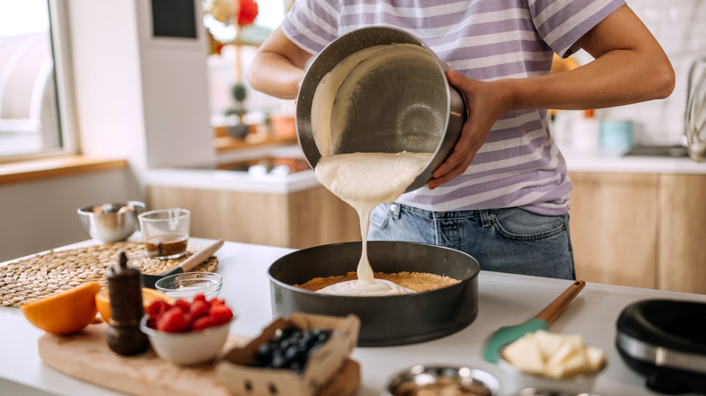 Person pouring cake mix in dark cake tin