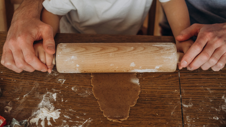 A child and parent rolling gingerbread dough