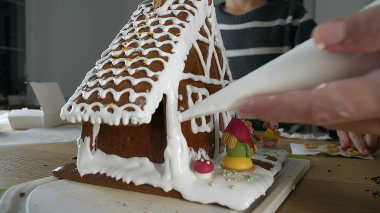 Hand piping royal icing onto a gingerbread house