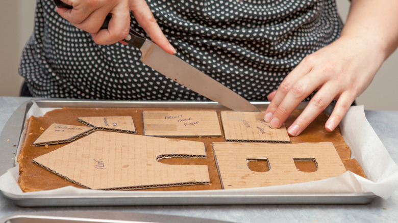 Hands cutting gingerbread house pieces using a template