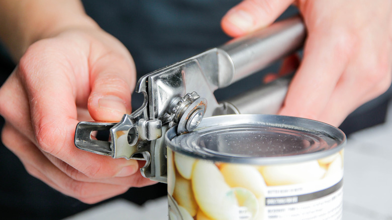 hands using can opener on can