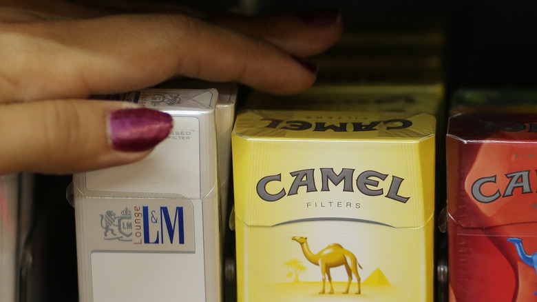 hands choosing from grocery store display of L&M and Camel cigarettes