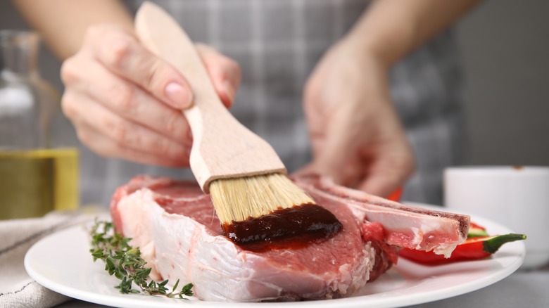 person brushing marinade on steak