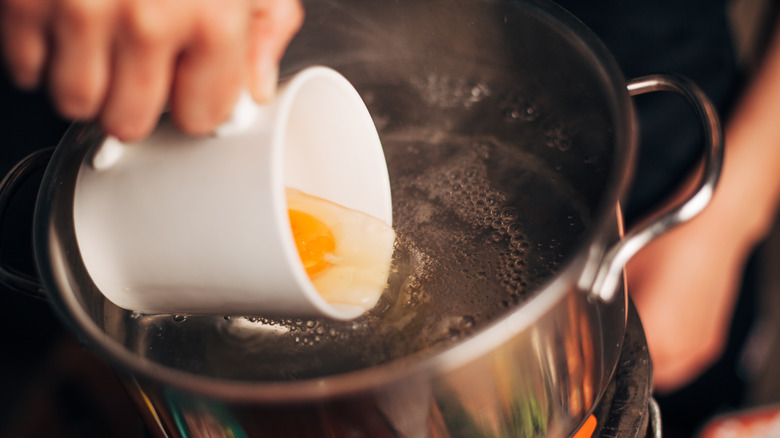 Person pouring an egg into poaching water