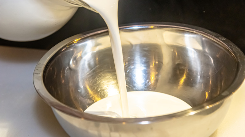 Heavy cream pouring into a stainless steel bowl