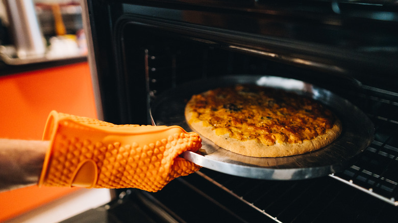 Hand in oven mitt pulling pizza from oven