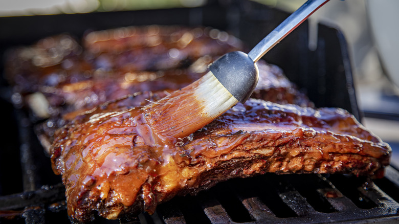 brushing barbecue sauce on grilled meat