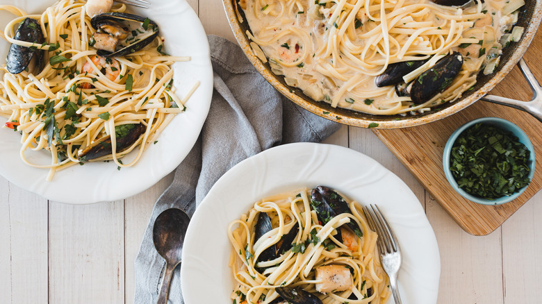 two plates of creamy seafood pasta and skillet on counter