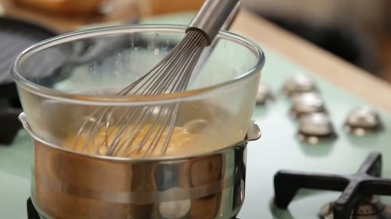 Bain-marie with eggs and balloon whisk on stove