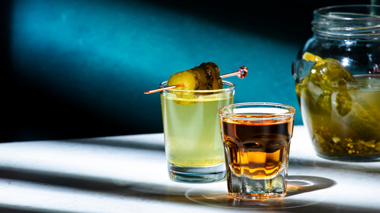 Shot glasses with whiskey and pickle juice, with blurred jar of pickles