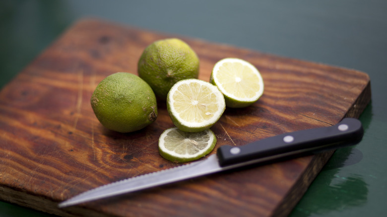 Whole and sliced limes on wooden board