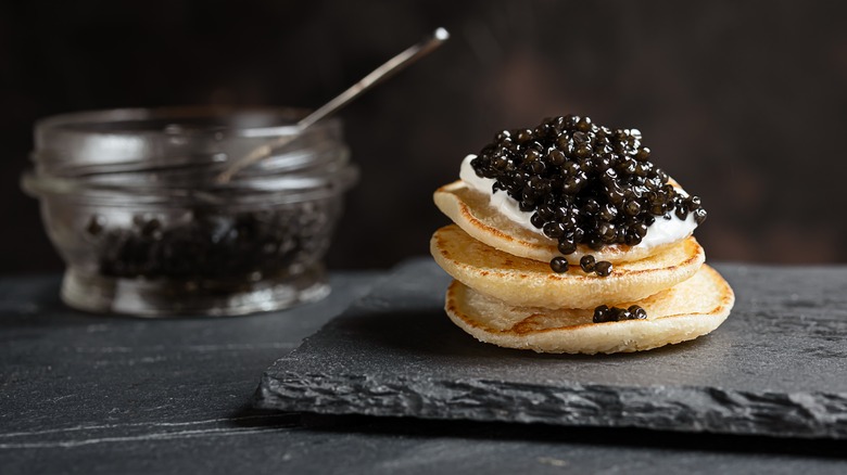 black caviar on small pancakes on black slate