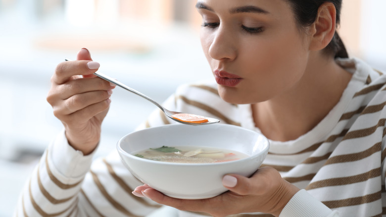 Woman blowing on soup spoon