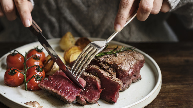 Knife and fork cutting into steak