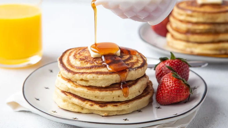 pouring syrup on stack of pancakes