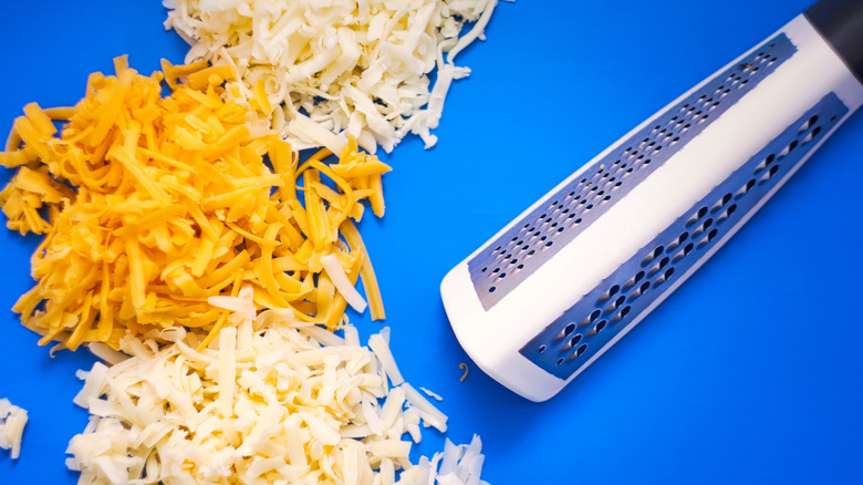 A variety of shredded cheeses next to a grater