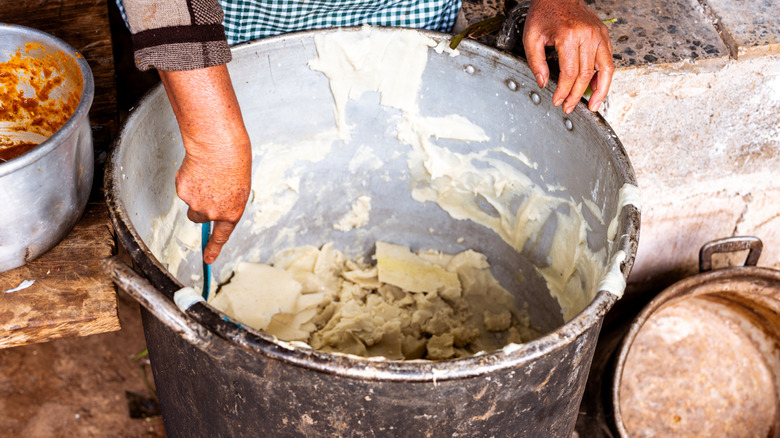 Hands mixing a large pot of masa