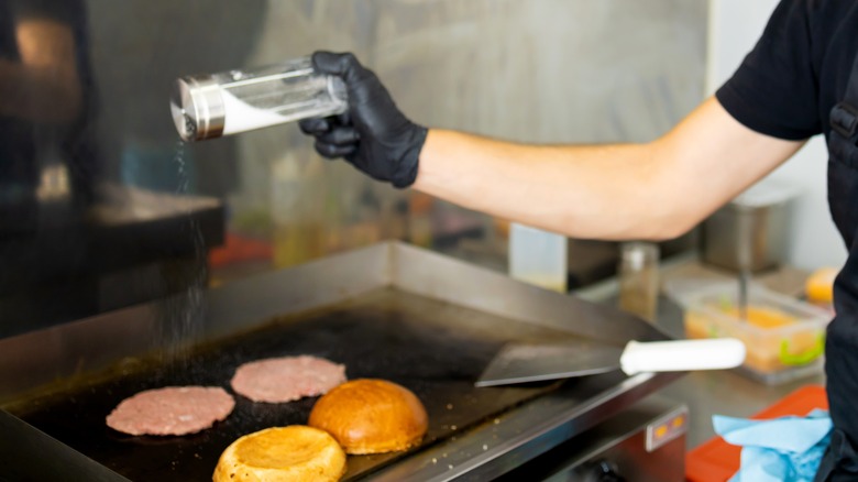 Seasoning smash burgers on griddle with salt and buns