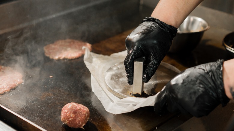 Gloved hands smashing burger under press