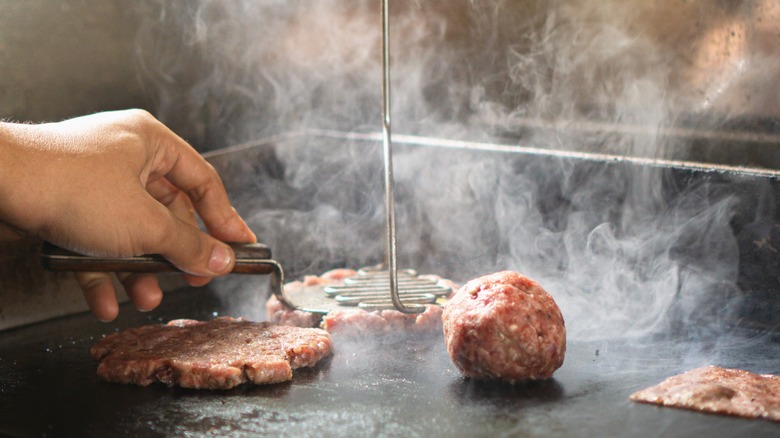 Smashing burgers on griddle with spatula and masher