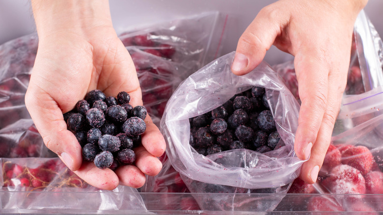 Hands scooping frozen blueberries from plastic bag