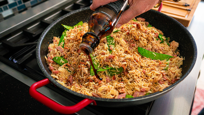 pouring soy sauce into a pan of fried rice