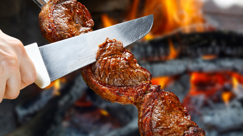 Person slicing Brazilian churrasco steak